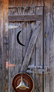 Weathered wood door to outhouse with moon cut-out