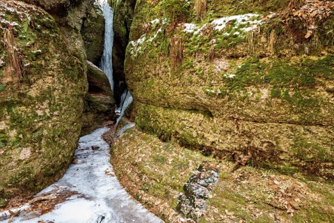 Narrow pass between moss-covered rocks with dammed ice and snow-covered ground, the Dragon Gorge