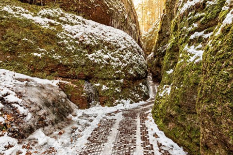 Snow-covered path between moss-covered rock faces in a quiet winter gorge, the Dragon Gorge near