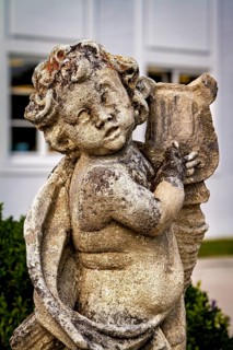 Weathered stone statue of an angel child with wings and background outdoors, stone statues in the