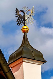 A wrought-iron heraldic animal on an onion dome in front of a blue sky with clouds, eagle figure on