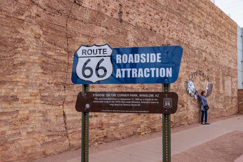 Woman posing for a photo behind roadside attraction sign at Standin' on the Corner Park in downtown