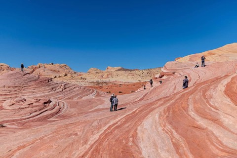 Hikers on a layered sandstone rock formation in the Fire Wave area of Valley of Fire State Park