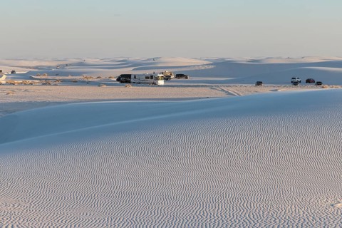 Cars and RVs in a parking area behind a rippled white gypsum sand dune at White Sands National Park