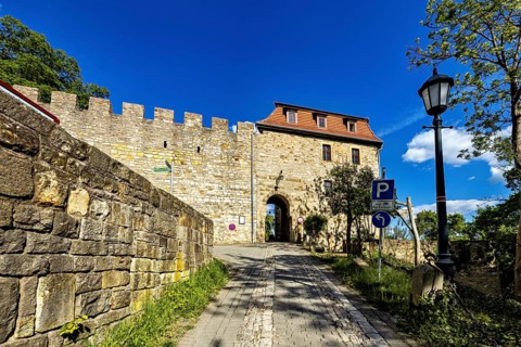 Stone entrance to a castle with cobblestone street and blue sky in the background, The Creuzburg in