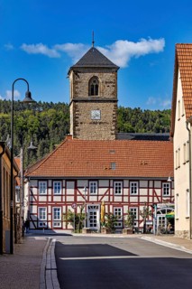 A half-timbered house with a church tower in the village, shining under a blue sky, The church