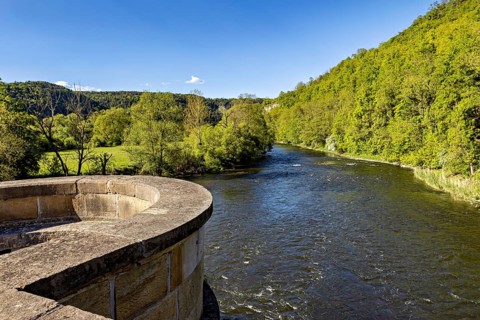 River next to a stone bridge, surrounded by forest under a blue sky, view from the historic Werra