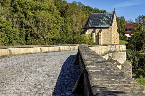 Close-up of a cobblestone road on a stone bridge leading to a chapel, surrounded by forest, The