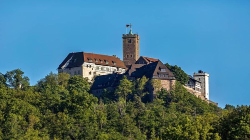 Castle with striking tower rises above green forests, Wartburg Castle near Eisenach in Thuringia