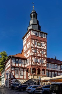 Half-timbered tower and historic buildings with parked cars under a blue sky, The town hall of