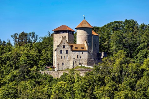 A medieval castle with two towers on a wooded hill under a blue sky, Normannstein Castle near