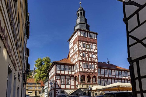 Half-timbered tower and surrounding buildings, seen through a narrow alley under a blue sky, The