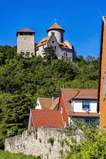 Half-timbered houses with red roofs in front of a castle on a wooded hill, Normannstein Castle near
