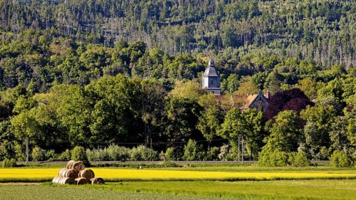 Landscape with church in the forest background and hay bales in the foreground, The church tower of