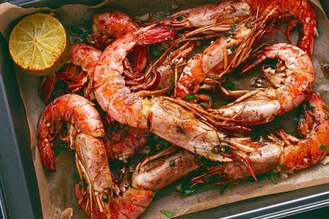Juicy grilled shrimp, placed on a baking sheet lined with parchment paper, garnished with herbs and