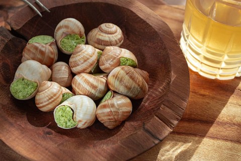 Snails cooked with herb oil on a wooden plate, served with white wine, natural light, no people