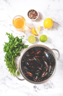 Fresh mussels, in a metal colander, with ingredients on the table, light background, no people