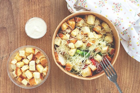 Caesar salad in a paper container, take it on the way, with sauce and croutons, on the table,
