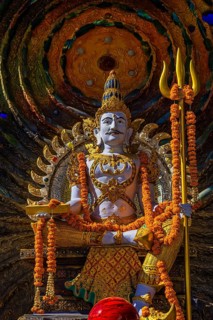 Hindu deity Shiva holding a trident, offerings in the foreground, a cosmic symbol in the back,