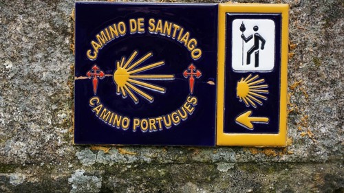 Guide on the Camino de Santiago with yellow arrow symbolism and cross, scallop on a stone wall,