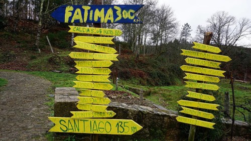 Various yellow signs show distances to Fatima and Santiago in a wooded landscape, pilgrims on the