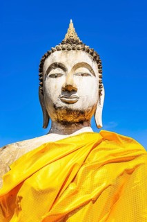 Stone Buddha statue decorated with yellow cloths, historic Buddhist temple complex, Ayutthaya,