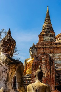 Stone Buddha statues, a high temple tower in the back, Prang, historic Buddhist temple complex,