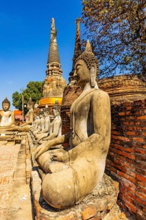 Stone Buddha statues sitting in a row, two temple towers in the back, Prang, historic Buddhist
