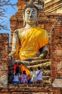 A family decorates a stone Buddha statue with yellow cloth, historic Buddhist temple complex,