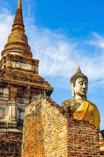 Stone Buddha statue decorated with yellow cloth, in the back a high temple tower, Prang, historic
