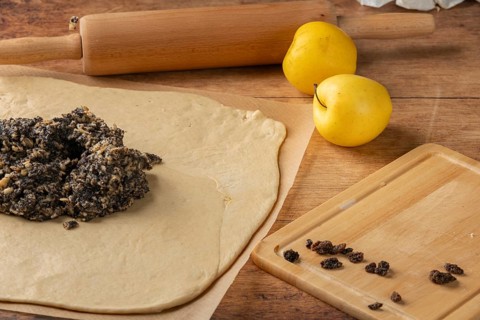 Rolled dough with poppy seeds and raisins on top, apple and rolling pin next to it