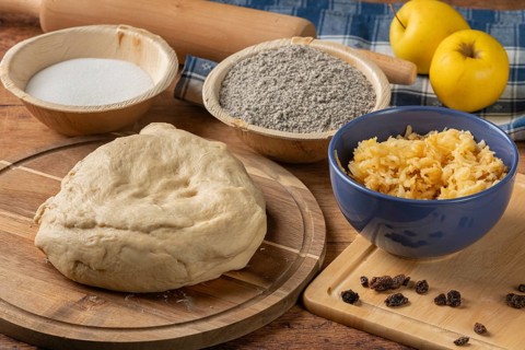 Dough prepared next to poppy seeds, grated apple and raisins on a wooden table