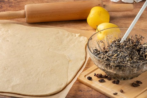 Rolled dough with poppy and raisin mixture in glass bowl, apple next to it