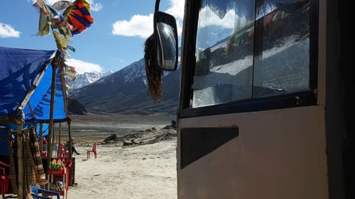 A bus and a colorful tent with pennants against a mountain backdrop, snack at a kiosk on a plateau