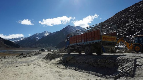 A truck parks on a mountain road with construction sites and mountains in the background, trekking