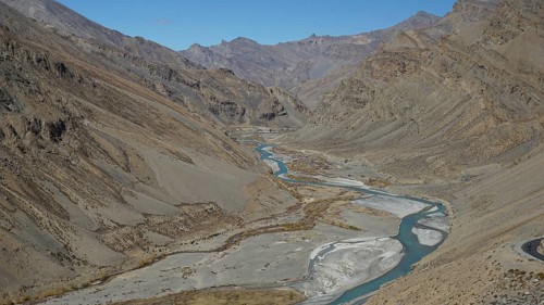 Shimmering blue Indus meanders through a barren valley under a blue sky, trekking in Ladakh,