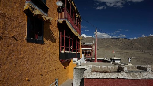 Façade of a Buddhist monastery casting shadows against a clear sky and mountain landscape, trekking