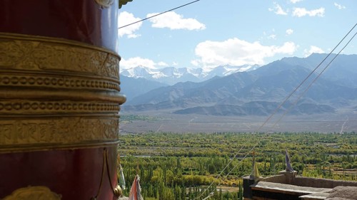 Large prayer wheel in foreground with view of snow-capped mountains and green valley, trekking in