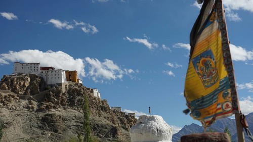 A Buddhist monastery on a hill with a fluttering prayer flag and majestic mountain views, trekking
