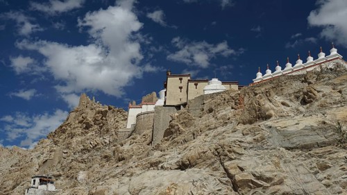 Buddhist monastery on a rocky slope under a bright blue sky with white clouds, trekking in Ladakh,