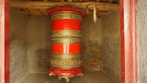 A large red prayer wheel decorated with decoration in a temple-like room, trekking in Ladakh,