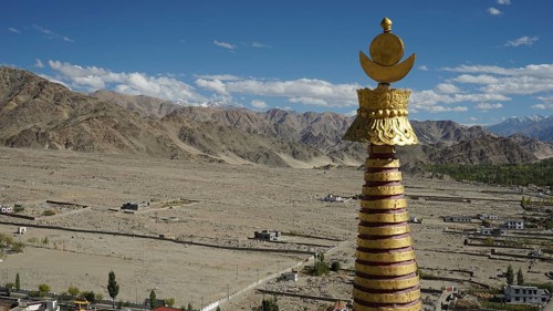 Golden stupa over a vast, mountainous landscape under a glowing sky, trekking in Ladakh, Himalayas,