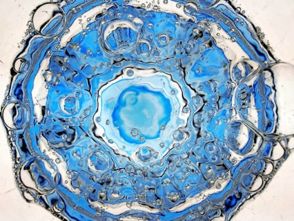 Rising carbon dioxide bubbles in a full water glass with a blue bottom seen from above, detail,