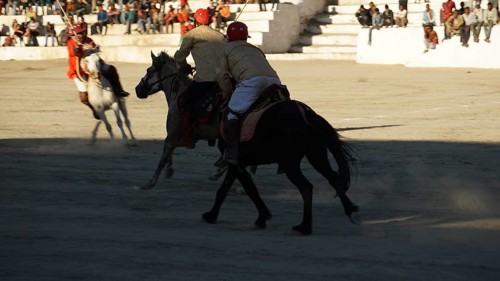 Polo players riding horses in a sand stadium in front of an audience in Leh, trekking in Ladakh,