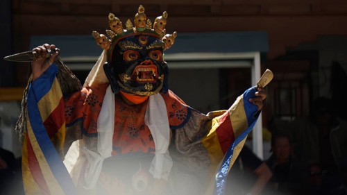 A mystical, colorfully dressed dancer wears a decorative mask during a ritual, Leh, trekking in
