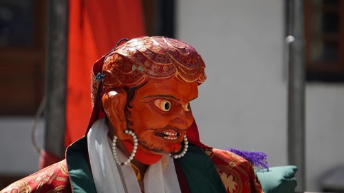 A vivid red-orange masked figure at a Buddhist ritual or dance in Leh, trekking in Ladakh,