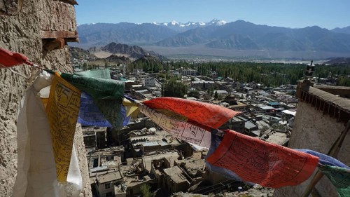 Colorful prayer flags fly over Leh with a mountainous landscape in the background, trekking in