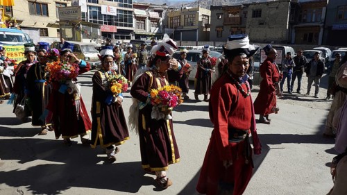 People wearing traditional garments carry flowers during a festive procession in Leh, trekking in