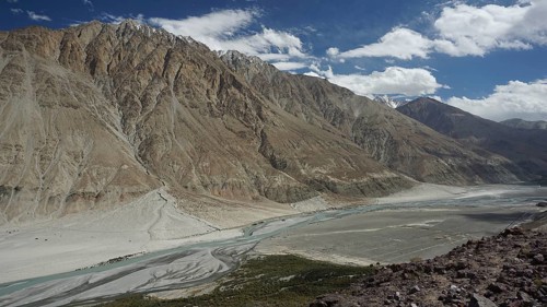 Mountain valley with river course between majestic mountain ranges under a lively sky, trekking in