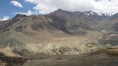 Dramatic mountain landscape with diverse rock formations, snow-capped peaks under a cloudy sky,